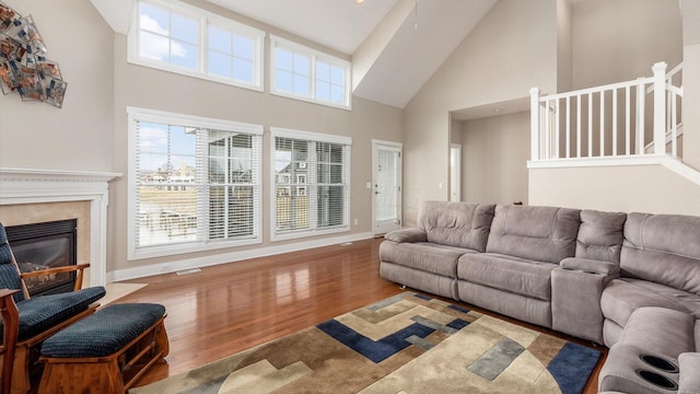 living area featuring a notable chandelier, a high end fireplace, wood finished floors, high vaulted ceiling, and baseboards