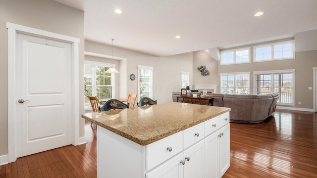 kitchen with wood-type flooring, a kitchen island, light stone counters, white cabinetry, and recessed lighting