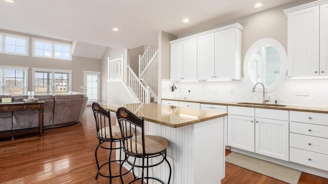 kitchen with a breakfast bar, hardwood / wood-style floors, open floor plan, light stone countertops, and a sink