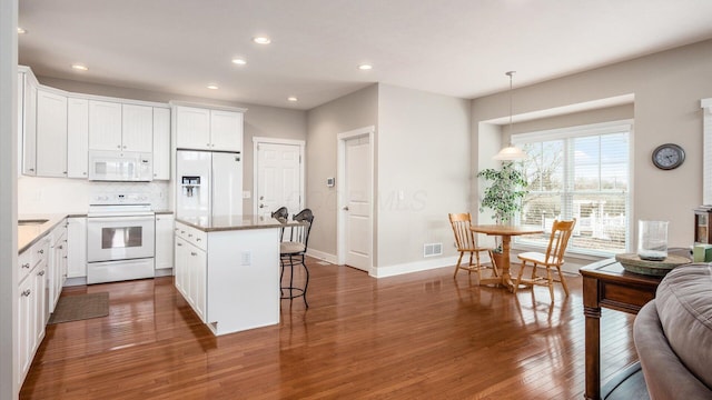 kitchen with white appliances, backsplash, a center island, hardwood / wood-style floors, and a kitchen bar