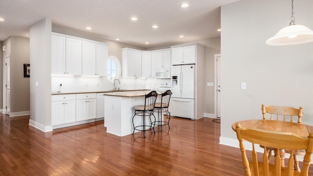 kitchen featuring white appliances, white cabinets, a kitchen island, and a kitchen bar