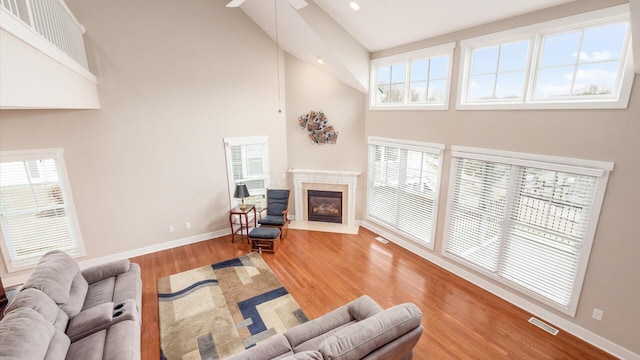 living room with a premium fireplace, wood finished floors, a towering ceiling, visible vents, and baseboards