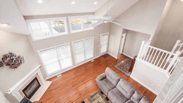 living room with high vaulted ceiling, wood finished floors, a fireplace with flush hearth, visible vents, and baseboards