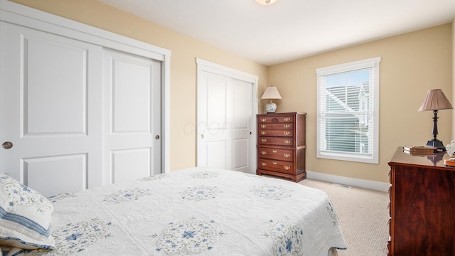 carpeted bedroom featuring visible vents, baseboards, and two closets