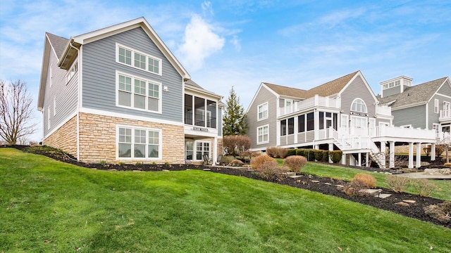 back of property with stone siding, a lawn, and a sunroom