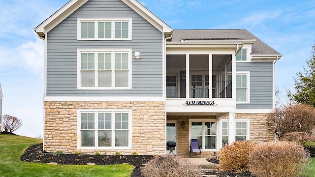 view of front of house featuring stone siding, a sunroom, and roof with shingles