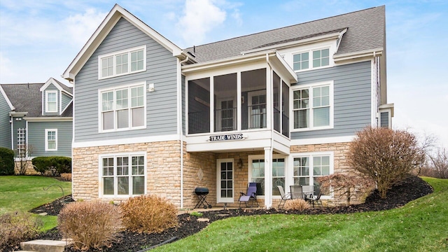 back of house featuring stone siding, a lawn, a sunroom, and roof with shingles