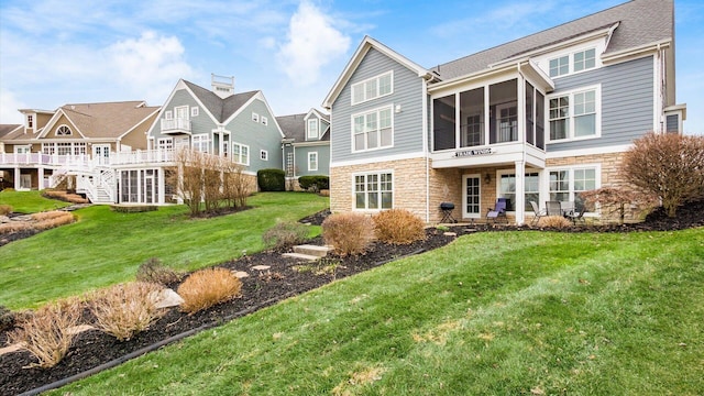 rear view of property with stone siding, a lawn, and a sunroom