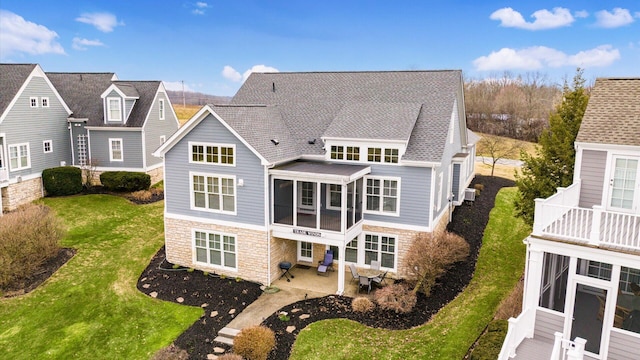 back of house featuring a yard, a patio, a shingled roof, a sunroom, and stone siding