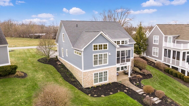 back of property featuring a shingled roof, stone siding, and a yard