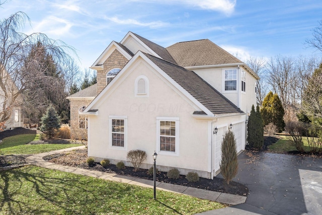 view of side of property featuring a garage, driveway, stone siding, roof with shingles, and stucco siding