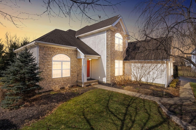 traditional home with a yard, roof with shingles, stone siding, and stucco siding