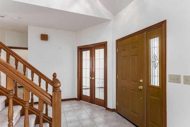 foyer entrance with french doors, stairway, light tile patterned flooring, a textured ceiling, and baseboards