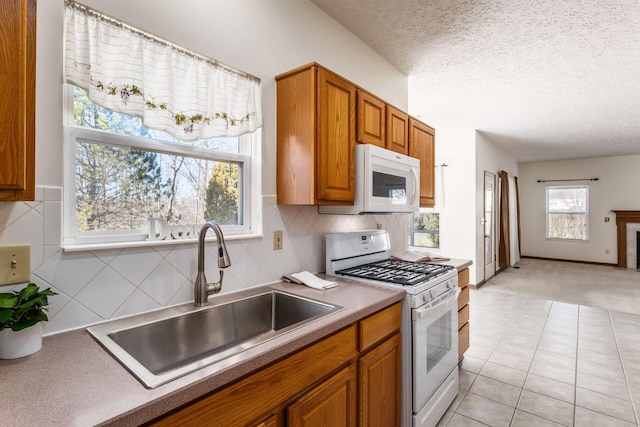 kitchen featuring a textured ceiling, white appliances, a sink, brown cabinets, and decorative backsplash