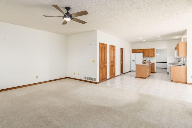 unfurnished living room featuring light carpet, baseboards, visible vents, a ceiling fan, and a textured ceiling