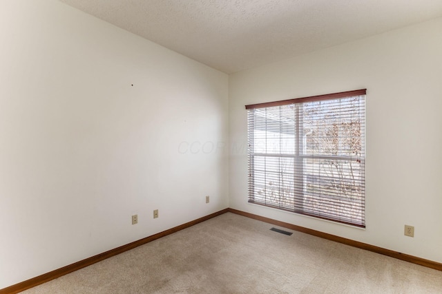 spare room with a textured ceiling, carpet, visible vents, and baseboards