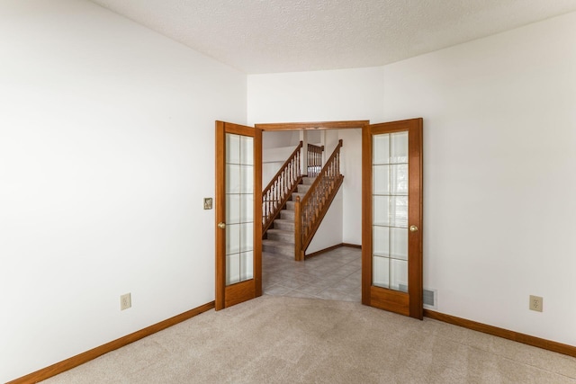 carpeted empty room featuring a textured ceiling, french doors, and baseboards