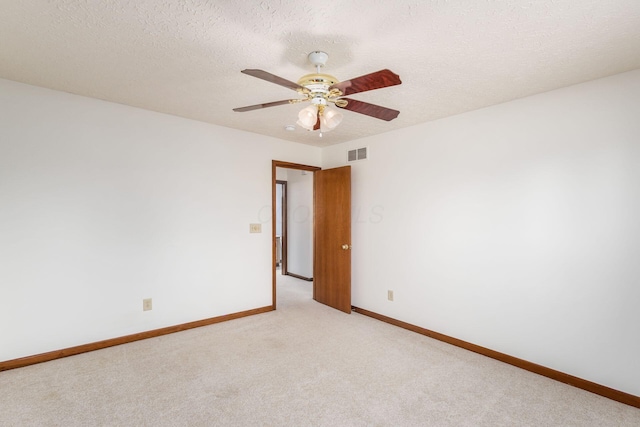 spare room with ceiling fan, a textured ceiling, light carpet, visible vents, and baseboards