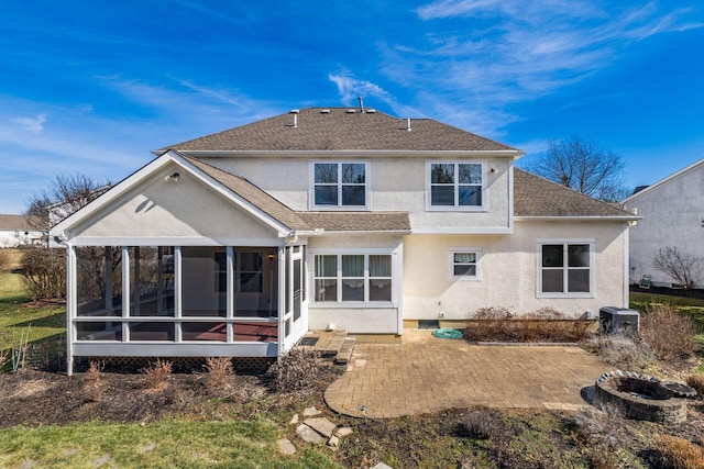 back of property featuring central AC unit, a shingled roof, a sunroom, stucco siding, and a patio area