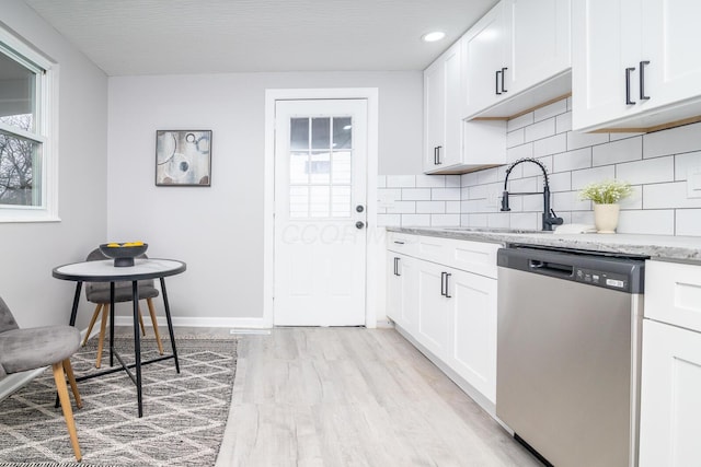 kitchen featuring stainless steel dishwasher, tasteful backsplash, a sink, and light stone counters