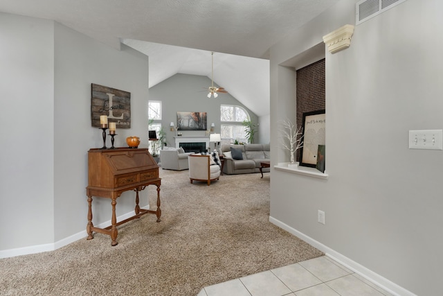 carpeted living room with visible vents, ceiling fan, tile patterned flooring, vaulted ceiling, and a fireplace