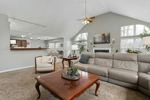 carpeted living room with high vaulted ceiling, a tile fireplace, rail lighting, and baseboards