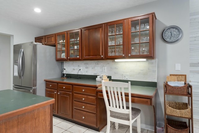 kitchen featuring light tile patterned floors, stainless steel fridge, glass insert cabinets, and decorative backsplash