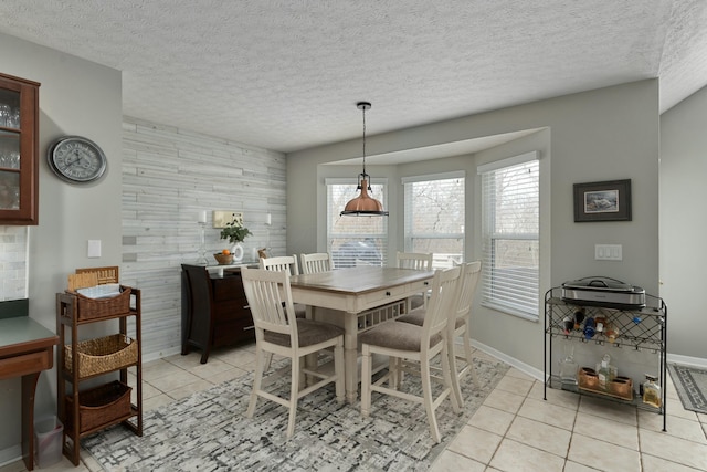 dining area with light tile patterned floors, wooden walls, baseboards, an accent wall, and a textured ceiling