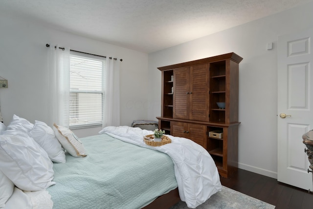 bedroom with a textured ceiling, dark wood finished floors, and baseboards