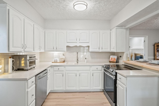 kitchen featuring stainless steel appliances, a sink, light wood-style flooring, and white cabinets