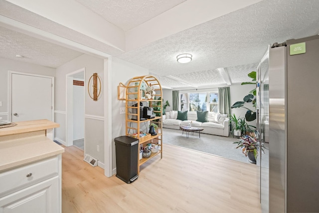 hallway with light wood finished floors, visible vents, and a textured ceiling