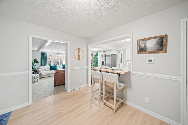 dining area featuring light wood finished floors, baseboards, visible vents, and a textured ceiling