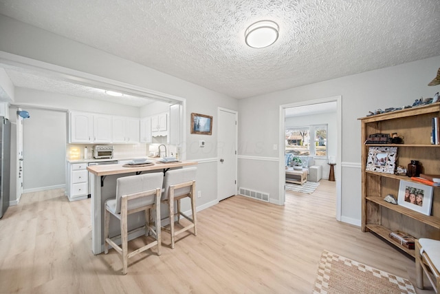 kitchen with a breakfast bar area, visible vents, light wood-style floors, white cabinets, and light countertops