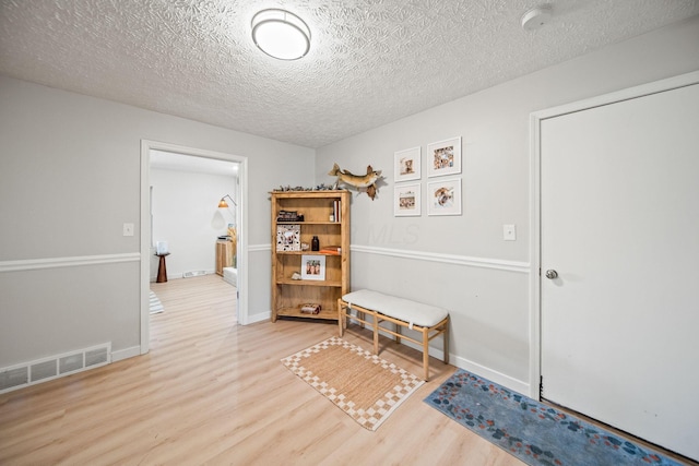 interior space with a textured ceiling, wood finished floors, visible vents, and baseboards