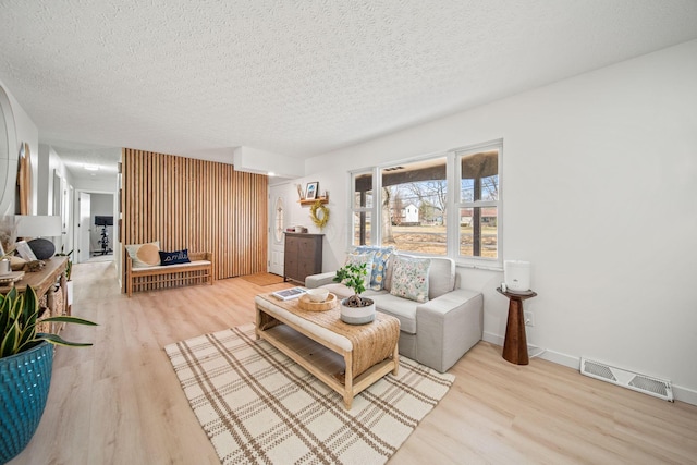 living area with baseboards, a textured ceiling, visible vents, and wood finished floors