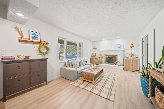 living area featuring a brick fireplace, a textured ceiling, baseboards, and wood finished floors