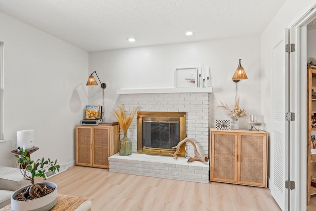 living room with recessed lighting, a brick fireplace, a textured ceiling, wood finished floors, and baseboards