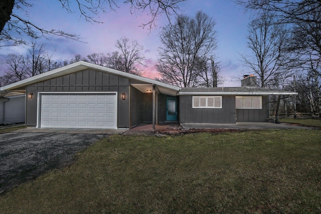 view of front of house featuring a garage, a chimney, aphalt driveway, a front lawn, and board and batten siding