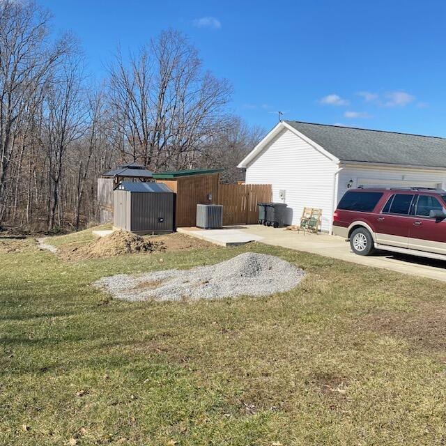 view of yard with cooling unit, an outdoor structure, fence, driveway, and a shed