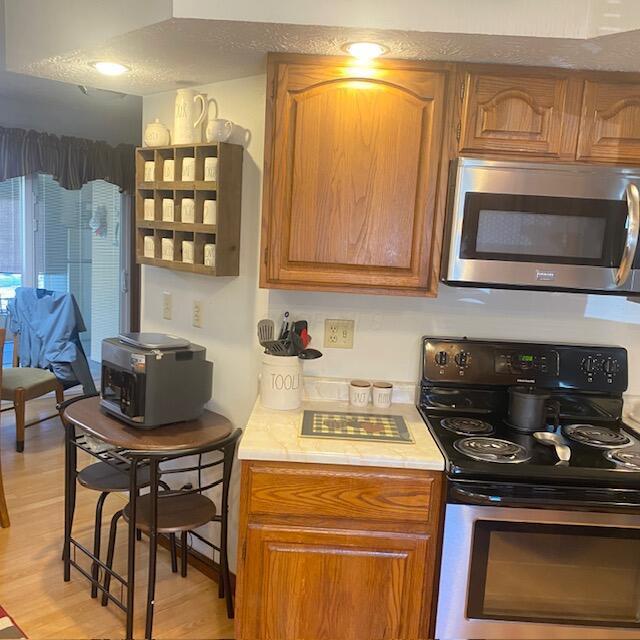 kitchen featuring stainless steel appliances, brown cabinets, light countertops, and light wood-style floors