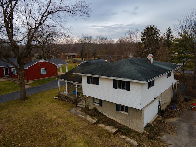 view of home's exterior featuring driveway, an attached garage, a chimney, and a lawn