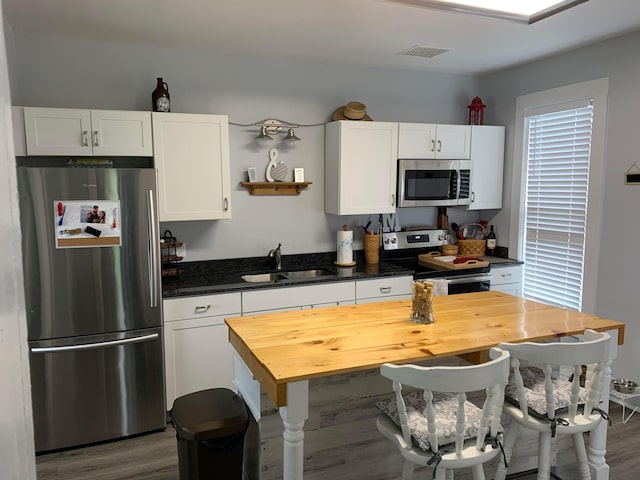 kitchen with visible vents, white cabinets, dark wood finished floors, stainless steel appliances, and a sink