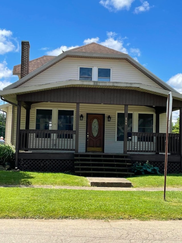 view of front of property with covered porch, roof with shingles, a chimney, and a front yard