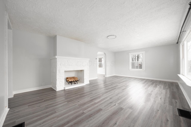 unfurnished living room featuring visible vents, a fireplace, arched walkways, and wood finished floors