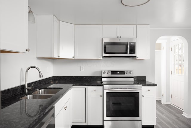 kitchen with light wood finished floors, stainless steel appliances, white cabinets, a sink, and dark stone counters