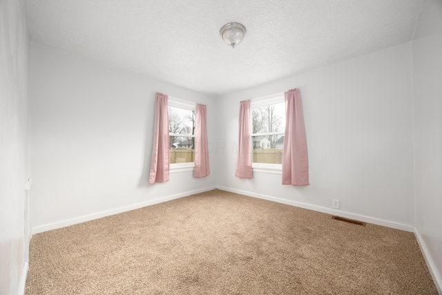 unfurnished room with a textured ceiling, carpet floors, visible vents, and baseboards