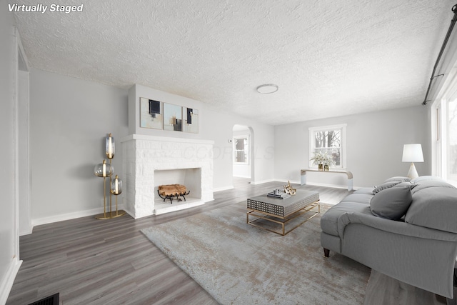 living room featuring arched walkways, visible vents, a brick fireplace, wood finished floors, and baseboards