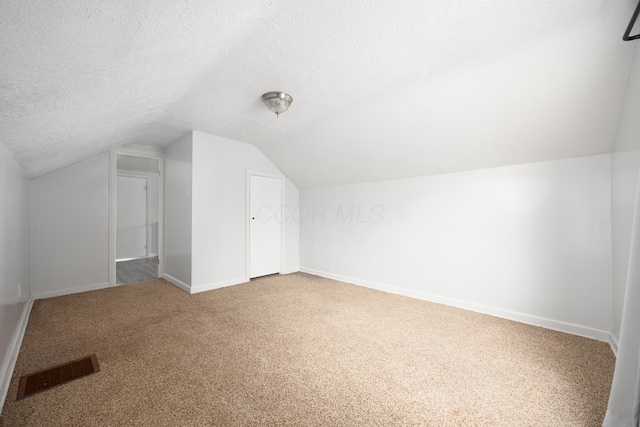 additional living space with a textured ceiling, lofted ceiling, carpet floors, visible vents, and baseboards