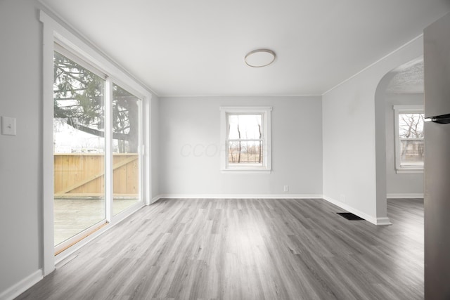 empty room featuring arched walkways, visible vents, baseboards, and wood finished floors