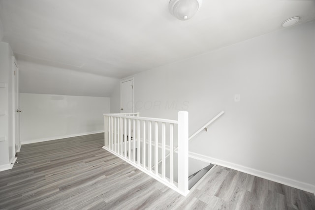 hall featuring baseboards, vaulted ceiling, an upstairs landing, and wood finished floors